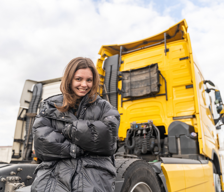 woman truck driver smiling in front of yellow truck